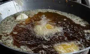 Intensywnie bulgoczący, rozgrzany olej na patelni, w którym smażą się kawałki ciasta. Widać, ile stopni ma rozgrzany olej na patelni po intensywności bąbelków.