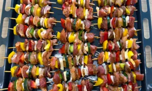 Szaszłyki drobiowe z warzywami (papryka, cukinia, cebula) na blasze, gotowe do pieczenia.