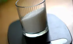 Szklanka z cukrem na wadze. Kluczowe jest ustalenie, ile cukru do zalewy peklującej, by uzyskać idealny smak.