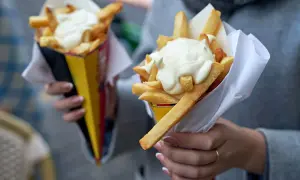 Dwie porcje frytek z majonezem w papierowych rożkach.