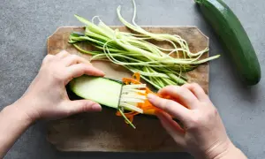 Ręce kroją cukinię w paski za pomocą spiralizera. Powstają długie, cienkie wstążki, idealne do sałatek i dań głównych.