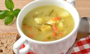 A miska zupy ogórkowej z ziemniakami i marchewką, obok kromka chleba i listki bazylii. Czy do zupy ogórkowej daje się czosnek?