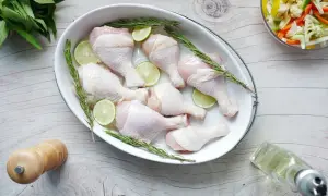 Surowe udka kurczaka w naczyniu z rozmarynem i limonką, gotowe do pieczenia. Zastanawiasz się, jak długo gotować udko z kurczaka?