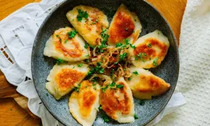 Złociste pierogi podsmażone na patelni, posypane szczypiorkiem i cebulką. Idealne na szybki obiad.