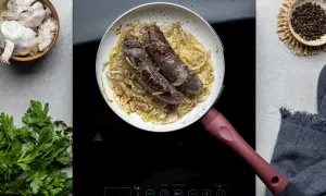 Kaszanka smażona na patelni z cebulą, obok czosnek, pieprz i natka pietruszki.
