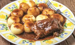 Kluski śląskie i pieczeń w sosie do karkówki, podane na talerzu z żółto-białym wzorem.