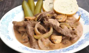 Strogonow z wołowiny z pieczarkami i cebulą, podany z ogórkami i bułeczkami. Idealny przepis, jak przygotować strogonowa.