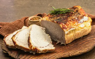Soczysty schab pieczony w piekarniku, pokrojony w plastry, z gałązką rozmarynu i miseczką przypraw.