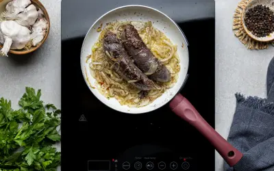 Kaszanka smażona na patelni z cebulą, obok czosnek, pieprz i natka pietruszki.