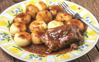 Kluski śląskie i pieczeń w sosie do karkówki, podane na talerzu z żółto-białym wzorem.