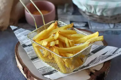Złota, chrupiąca frytka w metalowym koszyku na tle sosu i koszyka.