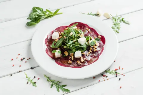 Eleganckie carpaccio z buraka z fetą, orzechami i rukolą, polane aromatycznym sosem.