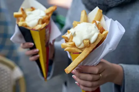 Dwie porcje frytek z majonezem w papierowych rożkach.