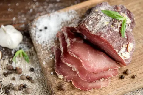 Pokrojone wędzone mięso na desce, obok czosnek, pieprz i sól. Idealne proporcje, by wiedzieć, ile cukru do peklowania mięsa na mokro.