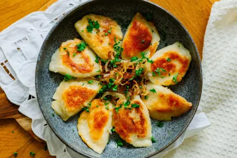 Złociste pierogi podsmażone na patelni, posypane szczypiorkiem i cebulką. Idealne na szybki obiad.