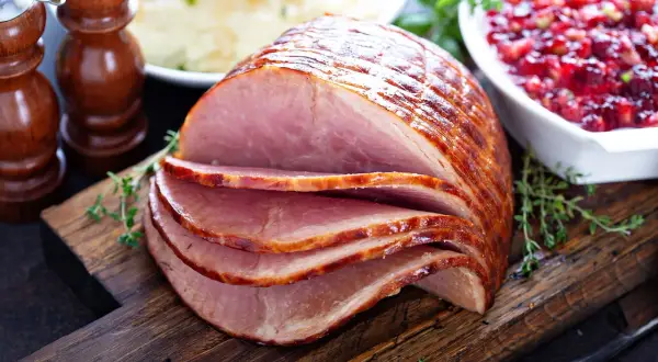 Pokrojona szynka z przyprawami, puree ziemniaczane i sos żurawinowy na desce.