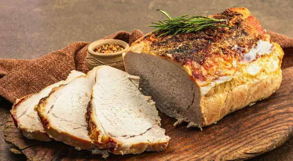 Soczysty schab pieczony w piekarniku, pokrojony w plastry, z gałązką rozmarynu i miseczką przypraw.