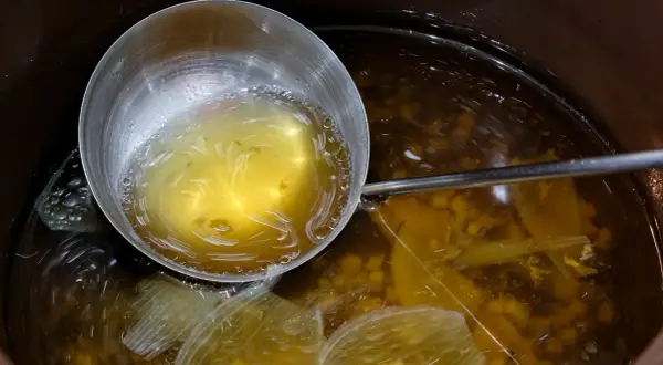 Nabierka z bulionem do grochówki, w garnku widać kawałki warzyw i przyprawy.