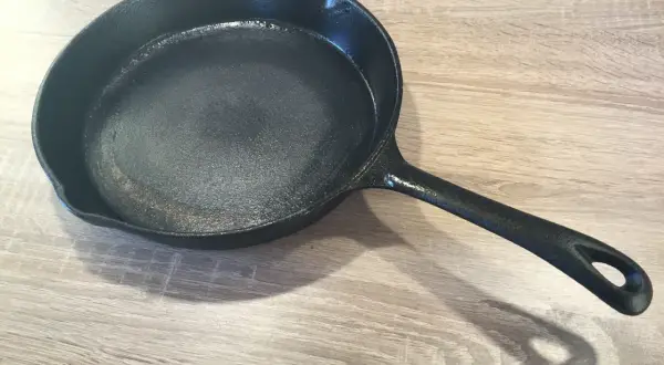Czarna, żeliwna patelnia na drewnianym blacie. Dowiedz się, jak przygotować patelnię żeliwną do pierwszego użycia i jak o nią dbać.