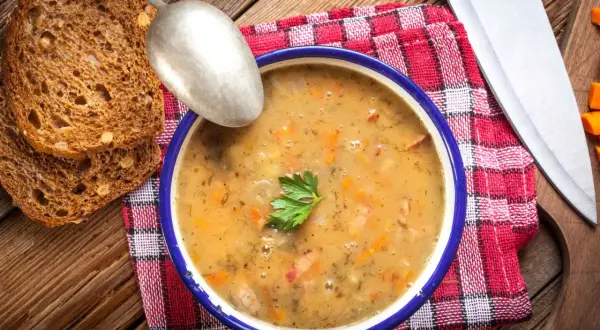 A miska grochówki z majerankiem, chlebem i łyżką. Kiedy dodać majeranek do grochówki? Pod koniec gotowania, by zachował aromat.