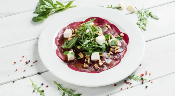 Eleganckie carpaccio z buraka z fetą, orzechami i rukolą, polane aromatycznym sosem.