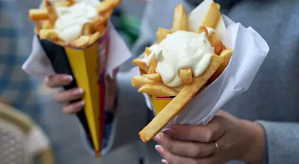 Dwie porcje frytek z majonezem w papierowych rożkach.