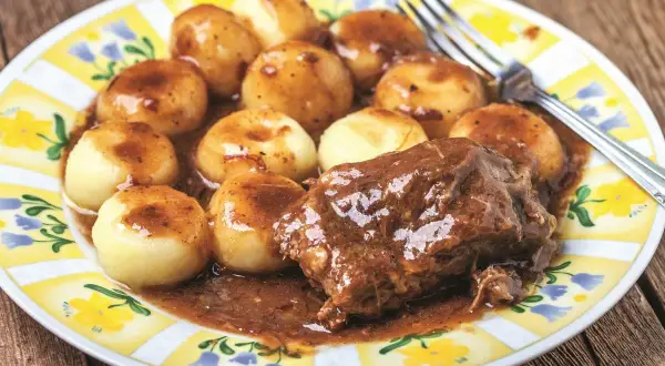 Kluski śląskie i pieczeń w sosie do karkówki, podane na talerzu z żółto-białym wzorem.