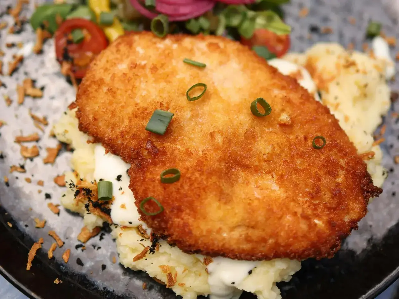 Złocisty kotlet schabowy na purée, posypany szczypiorkiem. Idealny sposób, jak odświeżyć kotlety schabowe na obiad.