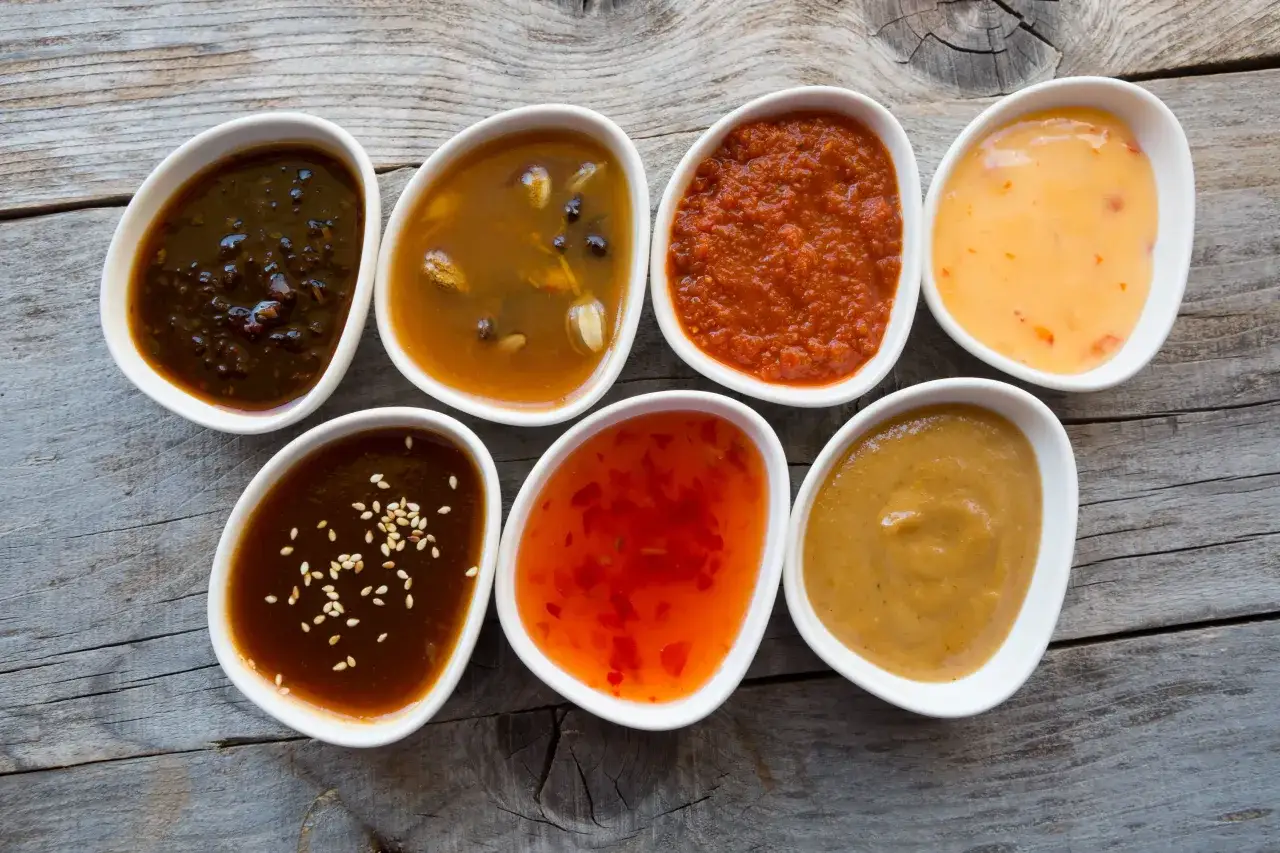 Siedem miseczek z różnymi sosami, idealnymi do karkówki: słodko-kwaśny, czosnkowy, pomidorowy, curry, sezamowy, chili i musztardowy.