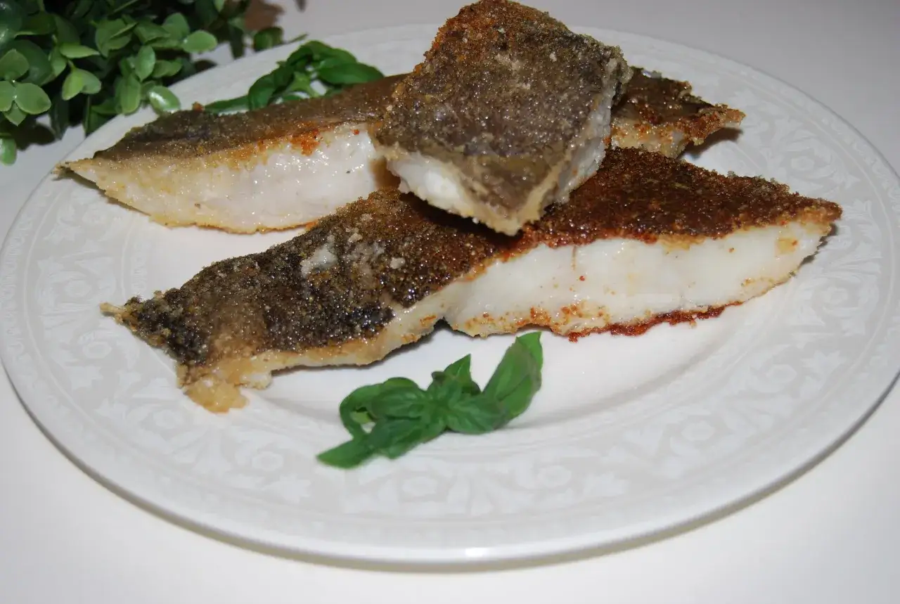 Usmażony halibut w panierce, podany na talerzu z bazylią. Idealny przykład, jak smażyć halibuta w dzwonkach.
