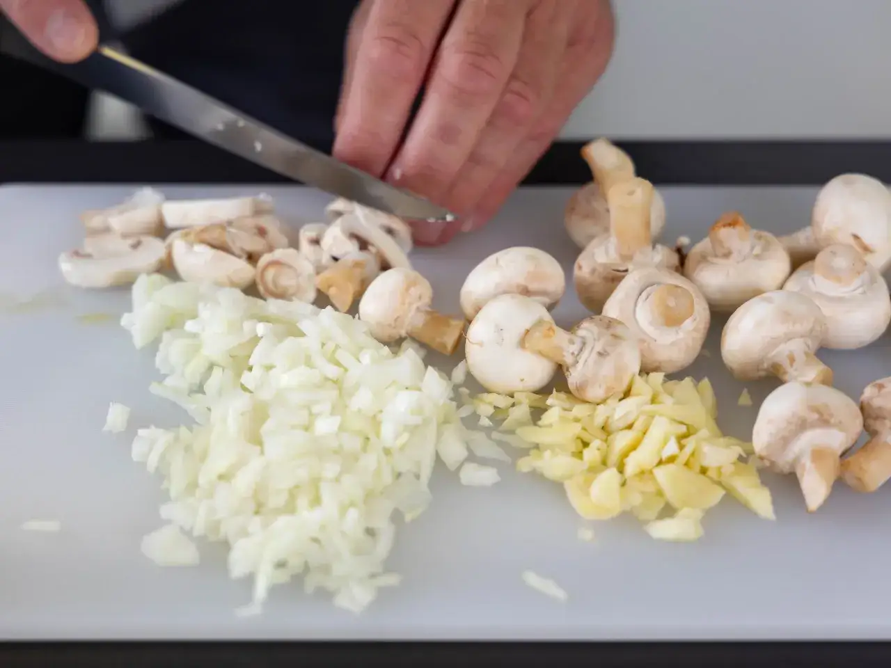 Na desce do krojenia leżą posiekana cebula, czosnek i pieczarki. Zastanawiasz się, ile gotować pieczarki?