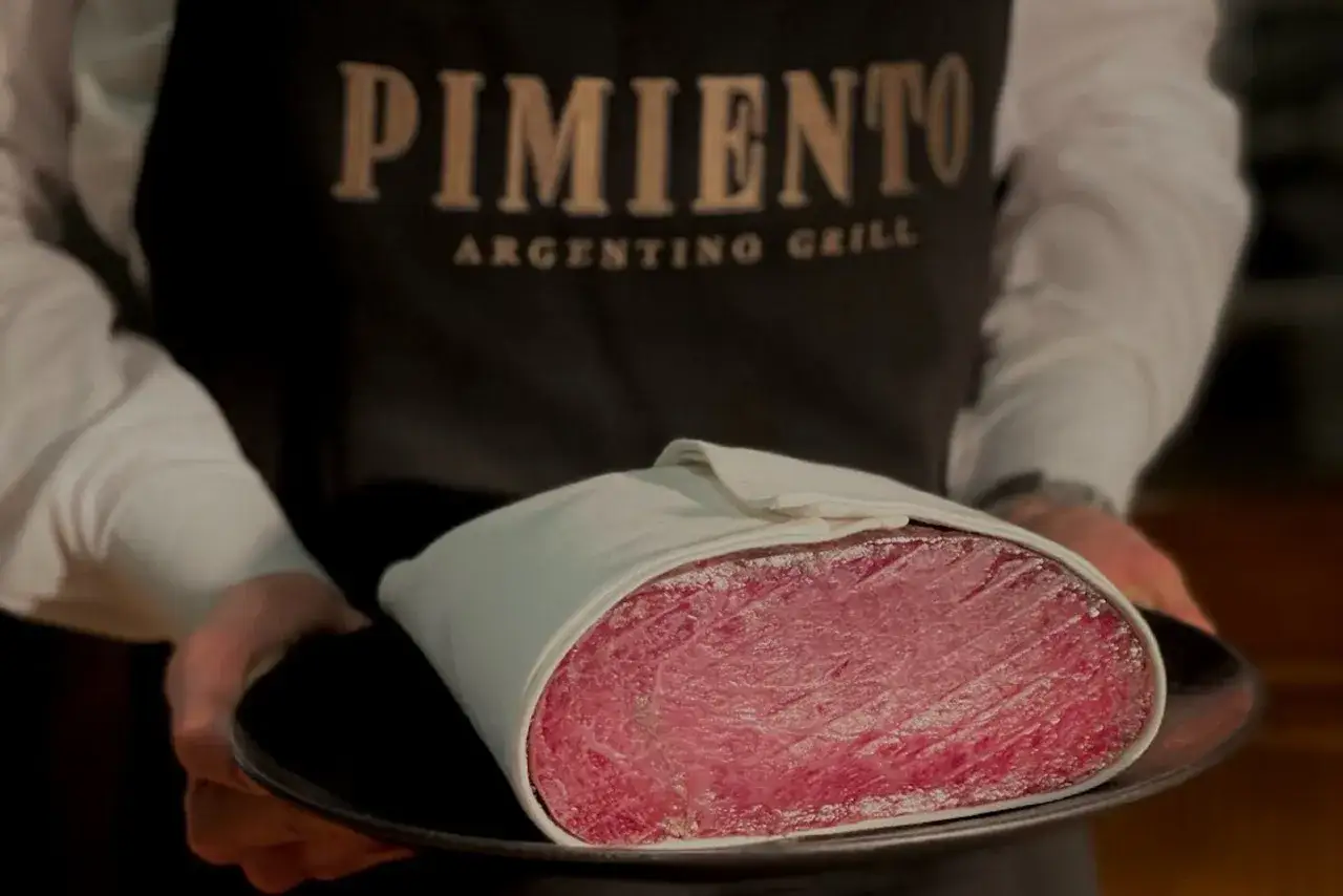 Pyszny kawałek wołowiny na talerzu, idealny na steka w Krakowie. Logo PIMIENTO ARGENTINO GRILL na fartuchu.