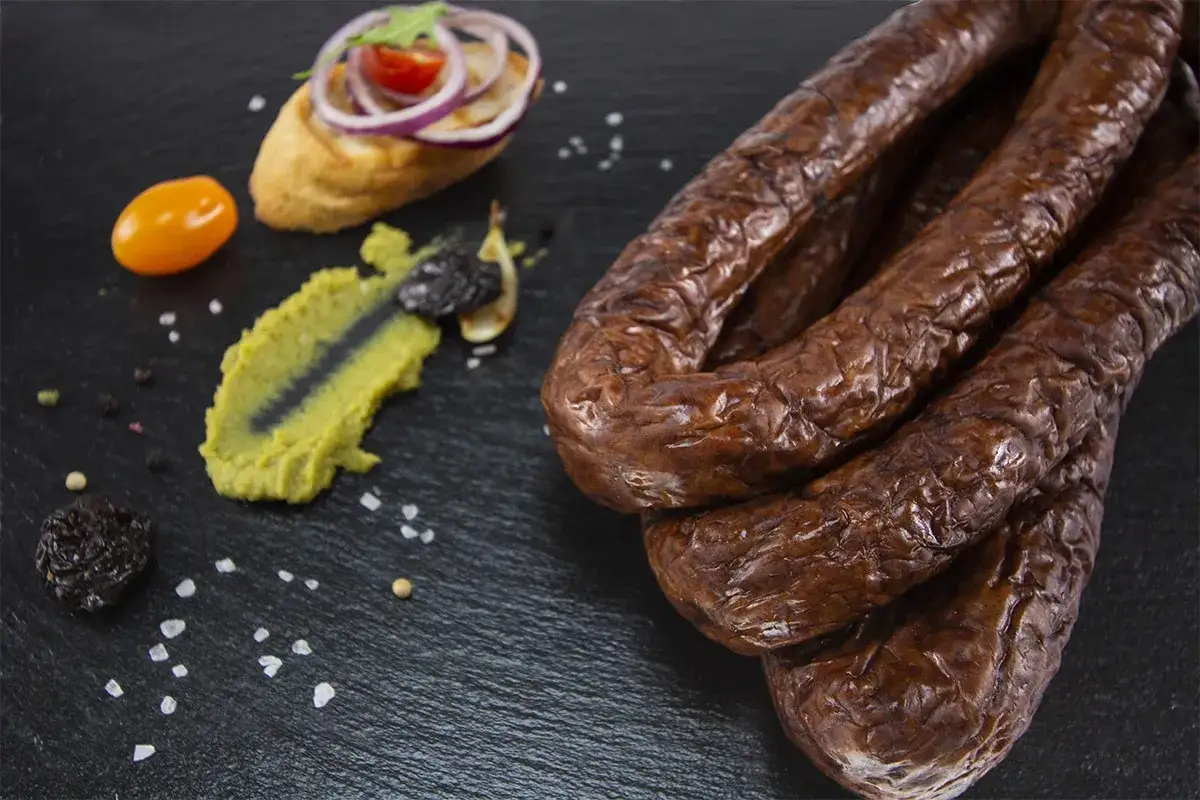 Kiełbasa z dzika z dodatkiem czosnku, podana z pastą warzywną, pomidorkiem i pieczywem.