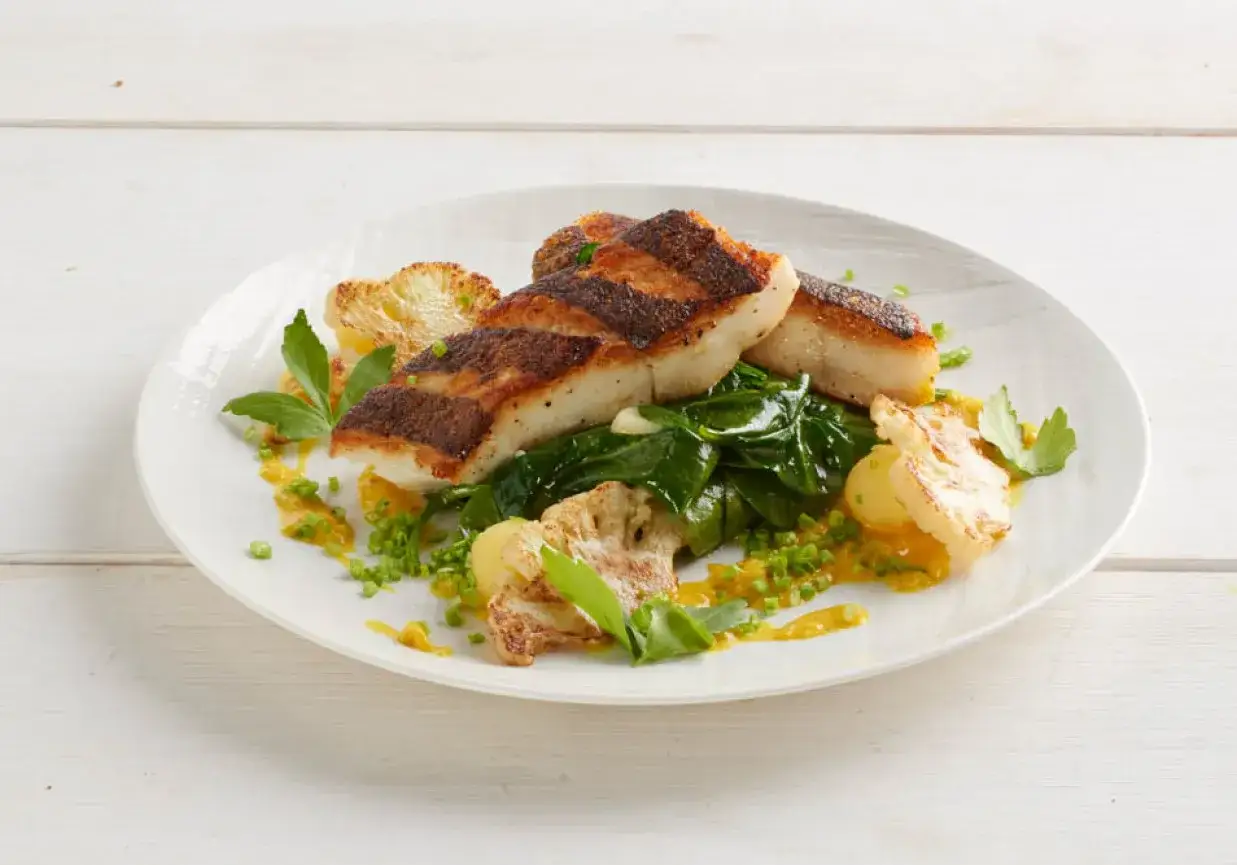 Smażony halibut z chrupiącą skórką, podany z duszonym szpinakiem, kalafiorem i żółtym sosem. Idealny przykład, jak przygotować halibuta do smażenia.