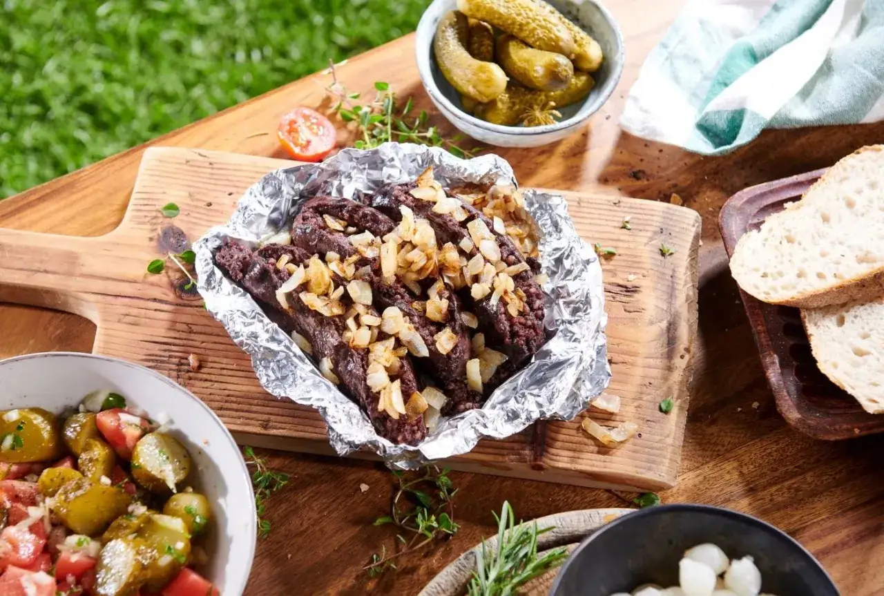 Kaszanka w folii z cebulką, idealna do odgrzania na grillu. Obok ogórki kiszone, sałatka i chleb.