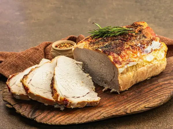 Soczysty schab pieczony w piekarniku, pokrojony w plastry, z gałązką rozmarynu i miseczką przypraw.