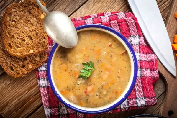 A miska grochówki z majerankiem, chlebem i łyżką. Kiedy dodać majeranek do grochówki? Pod koniec gotowania, by zachował aromat.