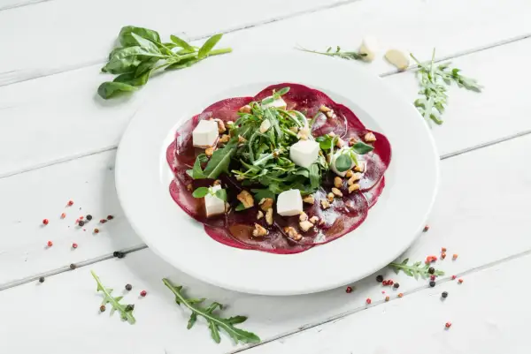 Eleganckie carpaccio z buraka z fetą, orzechami i rukolą, polane aromatycznym sosem.