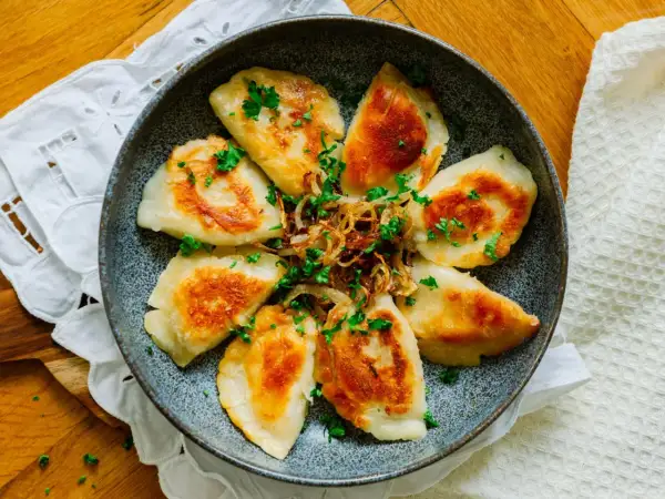 Złociste pierogi podsmażone na patelni, posypane szczypiorkiem i cebulką. Idealne na szybki obiad.